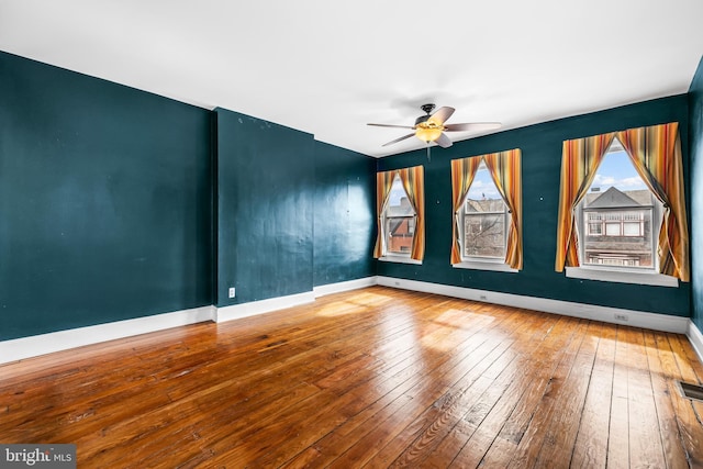 spare room with wood-type flooring, a ceiling fan, and baseboards