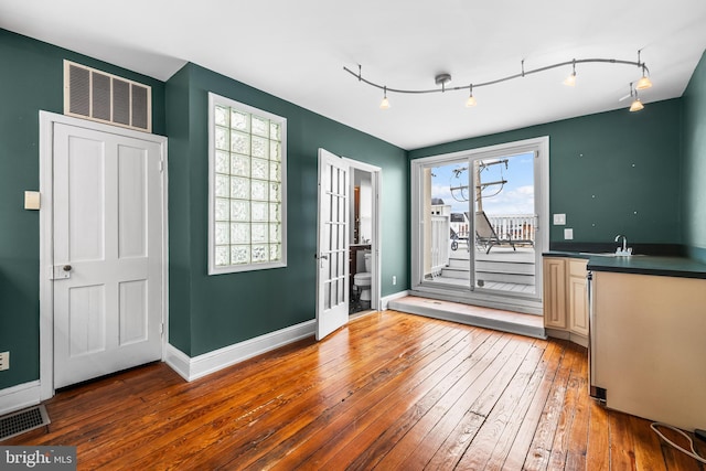 unfurnished dining area featuring visible vents, a sink, baseboards, and hardwood / wood-style flooring