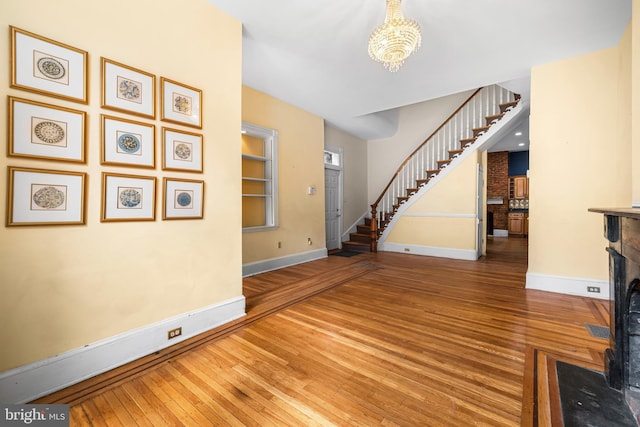 entryway featuring baseboards, wood-type flooring, a fireplace with flush hearth, stairs, and a chandelier