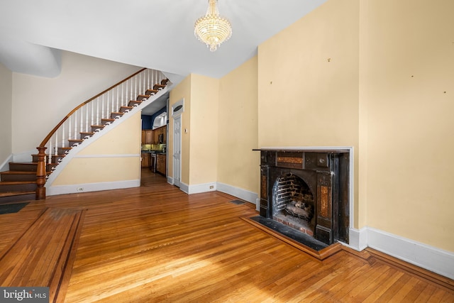 unfurnished living room featuring baseboards, hardwood / wood-style flooring, stairs, a fireplace, and a chandelier