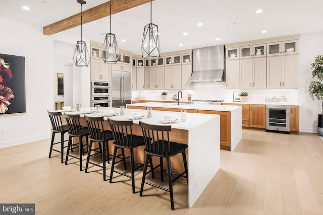 kitchen with beamed ceiling, appliances with stainless steel finishes, a large island, wall chimney exhaust hood, and wine cooler