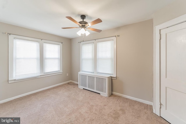 spare room featuring ceiling fan, light colored carpet, and radiator