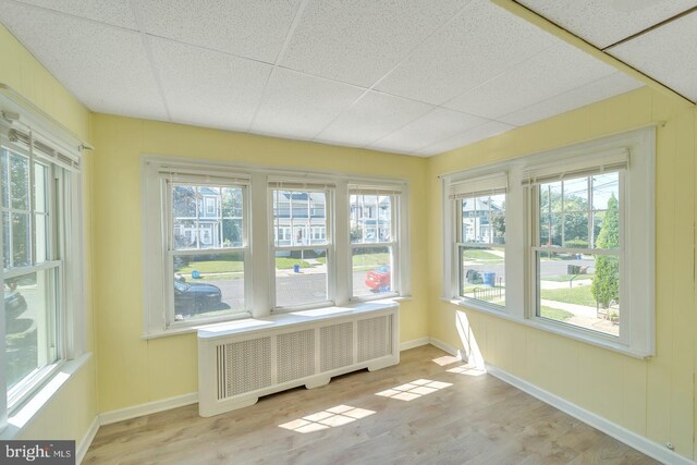 unfurnished sunroom with radiator heating unit, a healthy amount of sunlight, and a drop ceiling