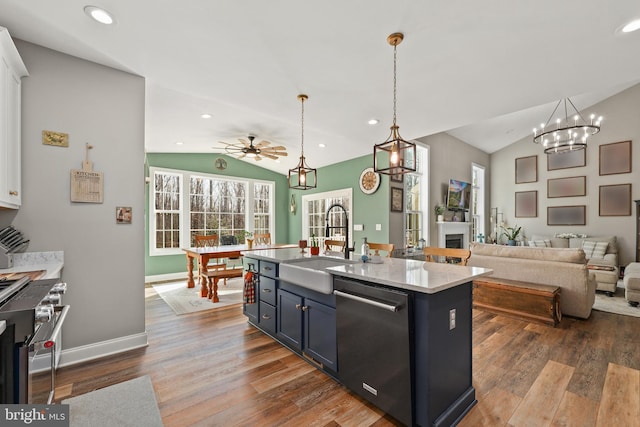 kitchen featuring vaulted ceiling, appliances with stainless steel finishes, sink, hanging light fixtures, and a center island with sink