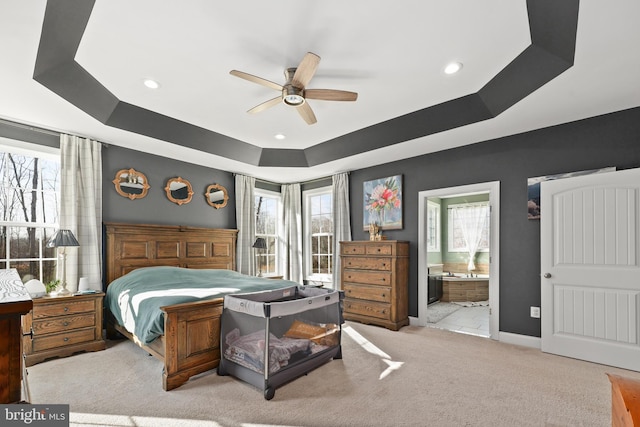 carpeted bedroom featuring ceiling fan, ensuite bath, a tray ceiling, and multiple windows