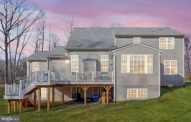 back house at dusk with a wooden deck and a lawn