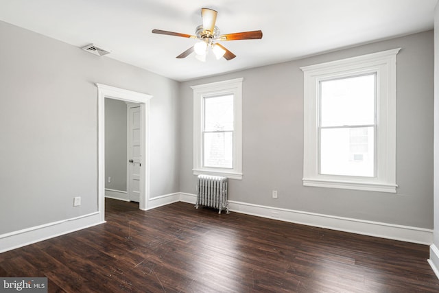 empty room featuring dark hardwood / wood-style floors, radiator, and ceiling fan