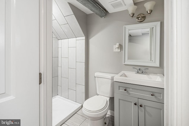 bathroom with toilet, tiled shower, and vanity