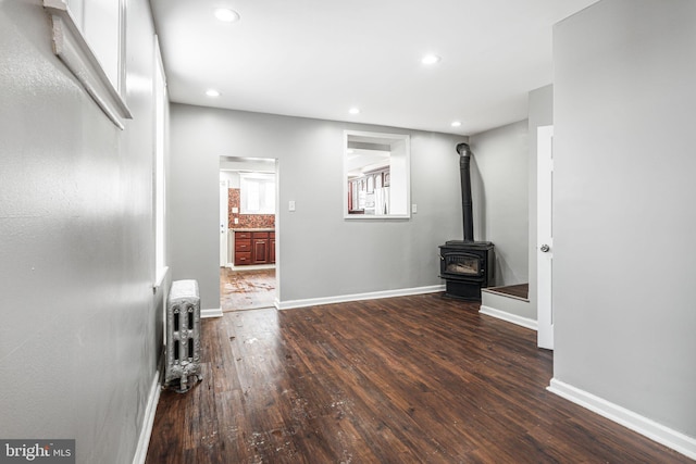 unfurnished living room featuring radiator heating unit, a wood stove, and dark hardwood / wood-style flooring