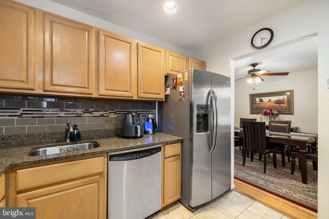 kitchen featuring stainless steel appliances, dark stone counters, sink, backsplash, and light tile patterned flooring