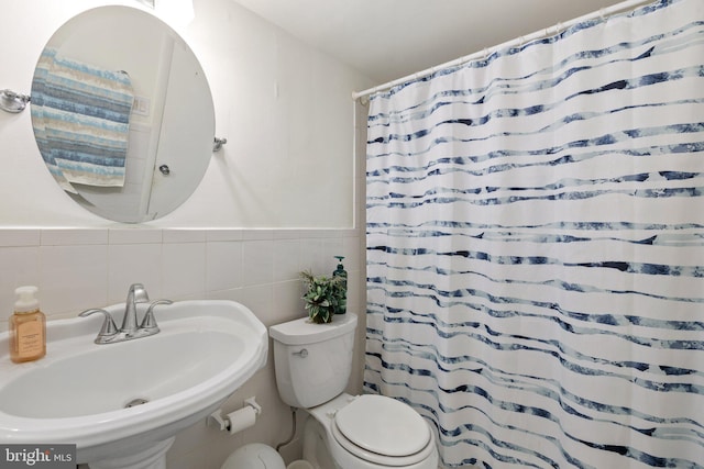 bathroom featuring sink, curtained shower, toilet, and tile walls