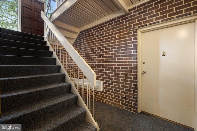 stairs featuring carpet floors, wooden ceiling, and brick wall