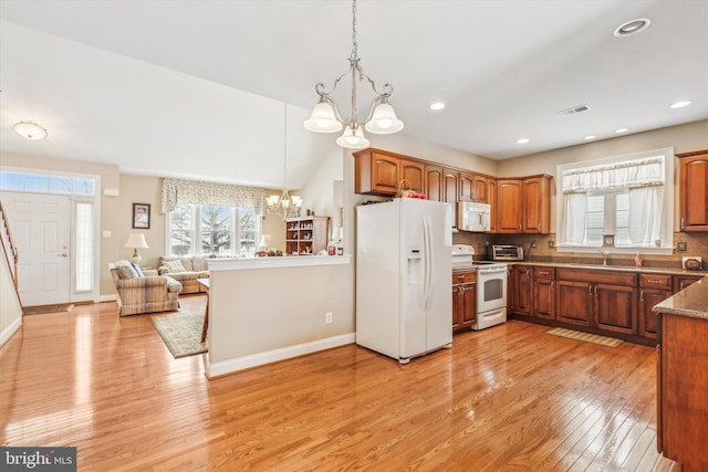 kitchen with sink, an inviting chandelier, light wood-type flooring, pendant lighting, and white appliances