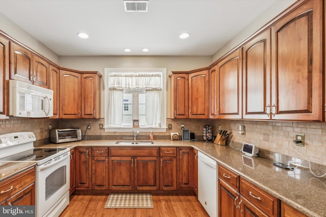 kitchen featuring sink, light wood-type flooring, stone counters, white appliances, and backsplash