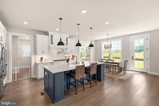 kitchen featuring pendant lighting, white cabinetry, a kitchen island with sink, tasteful backsplash, and stainless steel gas stovetop