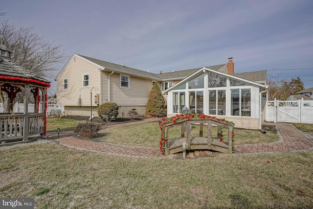 rear view of house with a gazebo, a lawn, and a sunroom