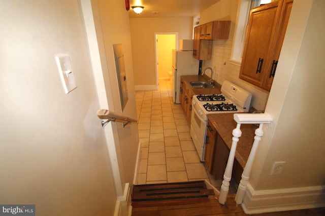 kitchen with white gas range, sink, backsplash, fridge, and light tile patterned floors