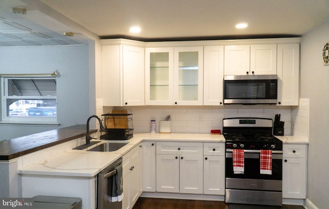 kitchen featuring sink, tasteful backsplash, kitchen peninsula, stainless steel appliances, and white cabinets