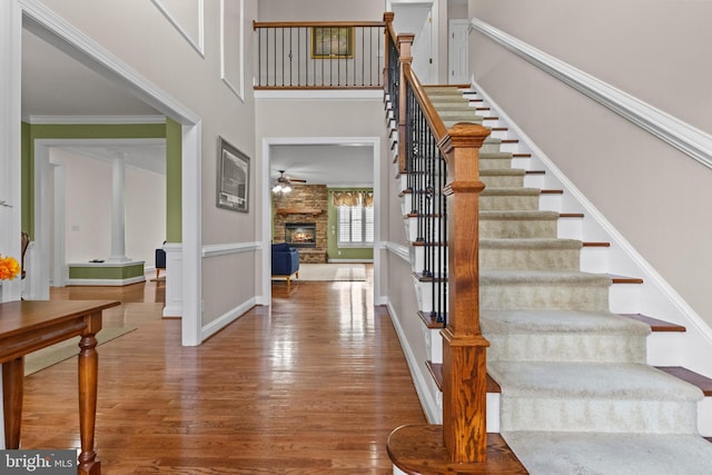 foyer entrance featuring ornamental molding, a towering ceiling, ceiling fan, a fireplace, and hardwood / wood-style floors