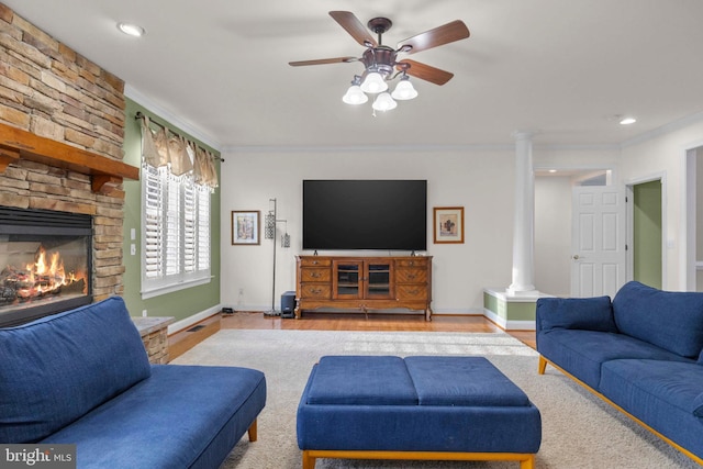 living room with crown molding, a stone fireplace, decorative columns, and light hardwood / wood-style flooring