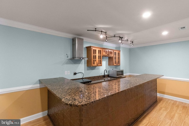 kitchen with sink, ornamental molding, kitchen peninsula, wall chimney exhaust hood, and light wood-type flooring