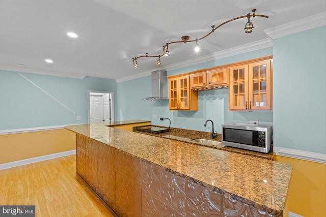 kitchen featuring stone counters, sink, ornamental molding, light hardwood / wood-style floors, and wall chimney exhaust hood