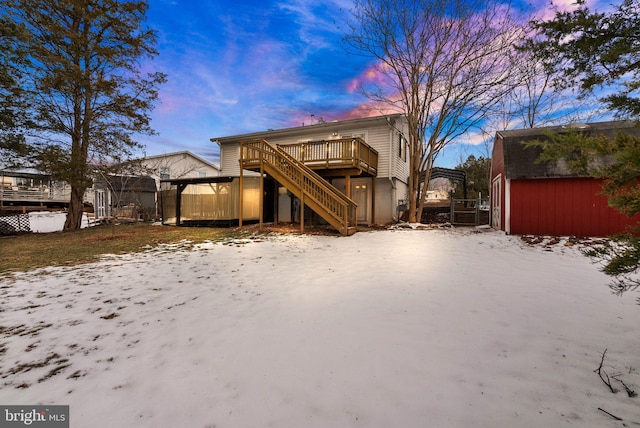 snow covered rear of property with a deck and a storage shed