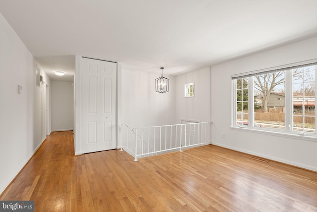 empty room with wood-type flooring and a notable chandelier