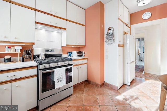 kitchen featuring stainless steel range with gas cooktop, white cabinets, white refrigerator, and light tile patterned floors