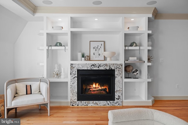 living area with built in features, wood finished floors, a fireplace, and ornamental molding