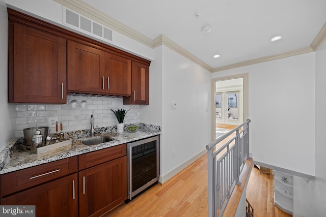 kitchen with beverage cooler, visible vents, ornamental molding, a sink, and light wood-type flooring