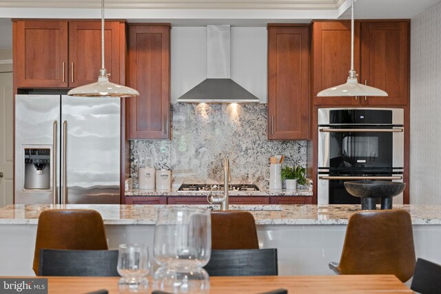 kitchen featuring stainless steel appliances, brown cabinets, backsplash, and wall chimney exhaust hood