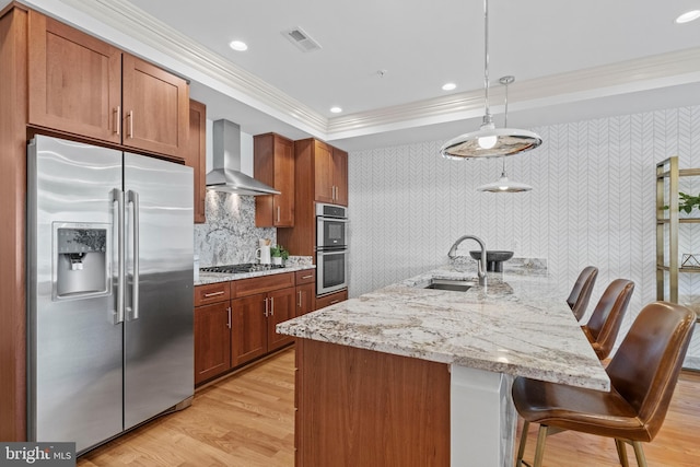 kitchen featuring visible vents, a sink, a tray ceiling, stainless steel appliances, and wall chimney exhaust hood