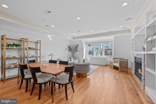 dining space featuring visible vents, wallpapered walls, light wood-type flooring, ornamental molding, and a premium fireplace