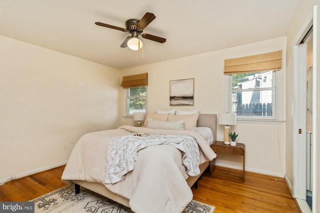 bedroom featuring a ceiling fan, multiple windows, baseboards, and light wood-type flooring