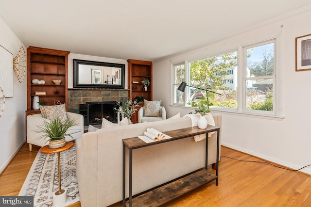 living area with a tiled fireplace, light wood-type flooring, baseboards, and ornamental molding