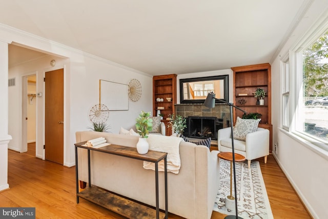 living room featuring light wood-style flooring, a fireplace, visible vents, and baseboards