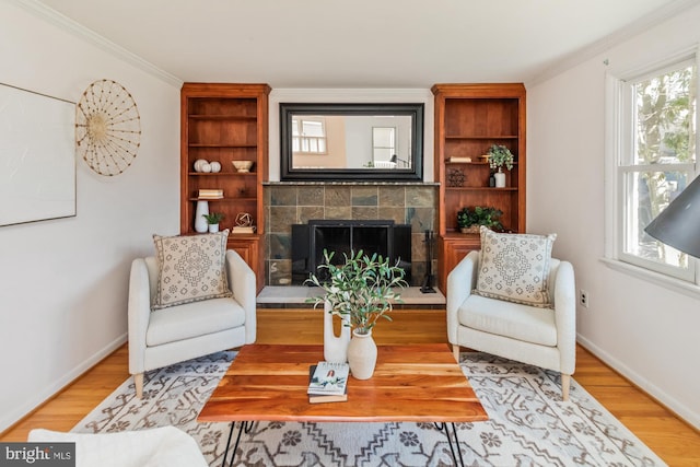 living area featuring crown molding, baseboards, light wood finished floors, and a tile fireplace