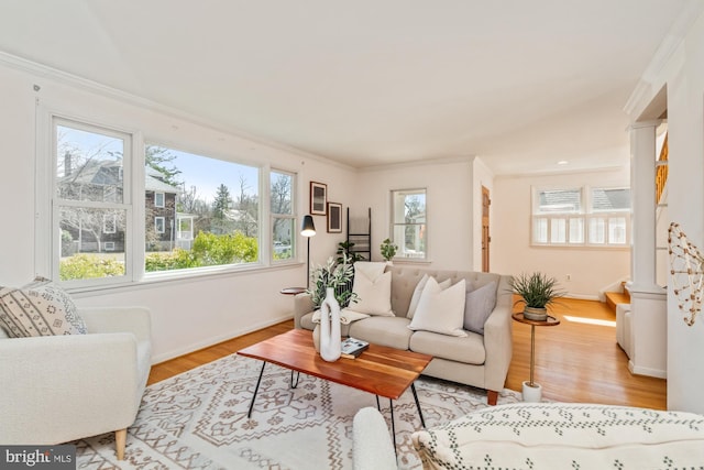 living area featuring ornate columns, wood finished floors, baseboards, and ornamental molding