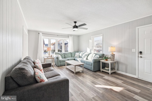 living room with a textured ceiling, wood walls, ceiling fan, and light wood-type flooring