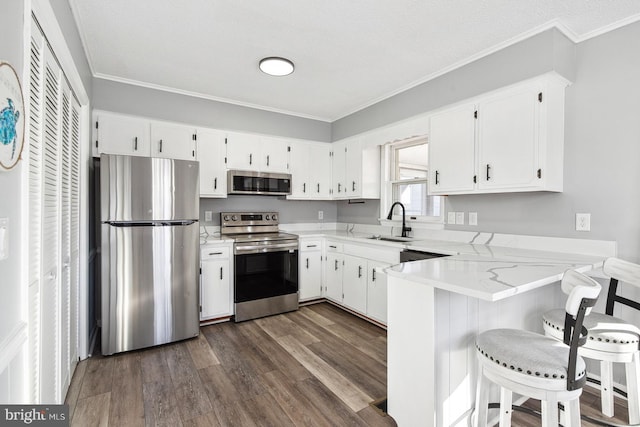 kitchen with sink, appliances with stainless steel finishes, white cabinetry, a kitchen bar, and kitchen peninsula