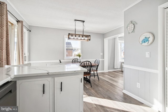 kitchen with white cabinetry, light wood-type flooring, hanging light fixtures, ornamental molding, and a textured ceiling