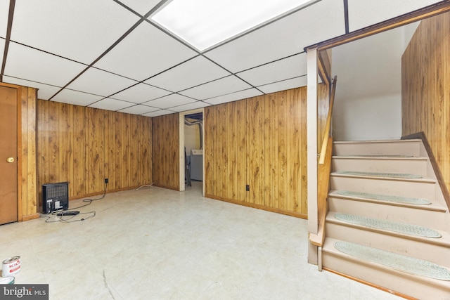 basement with a paneled ceiling, wooden walls, and washer / clothes dryer