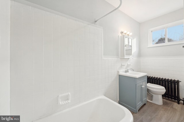 bathroom with toilet, radiator, wood-type flooring, tile walls, and vanity