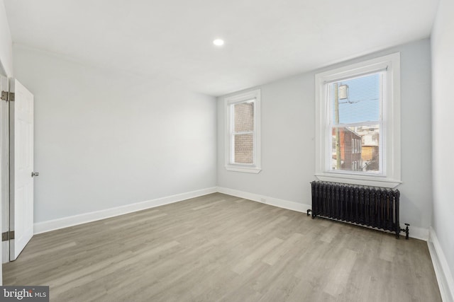 unfurnished room featuring radiator heating unit and light hardwood / wood-style floors