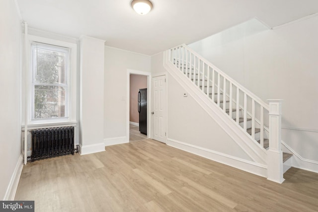 stairway featuring wood-type flooring, radiator heating unit, a healthy amount of sunlight, and ornamental molding