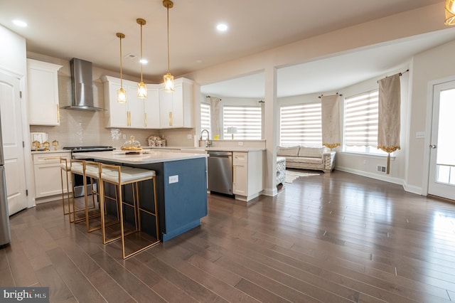 kitchen featuring wall chimney range hood, appliances with stainless steel finishes, a kitchen island, white cabinets, and a kitchen bar