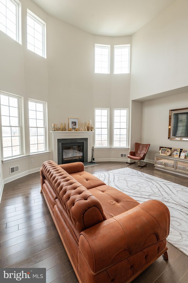 living room featuring a towering ceiling, a wealth of natural light, and dark hardwood / wood-style floors