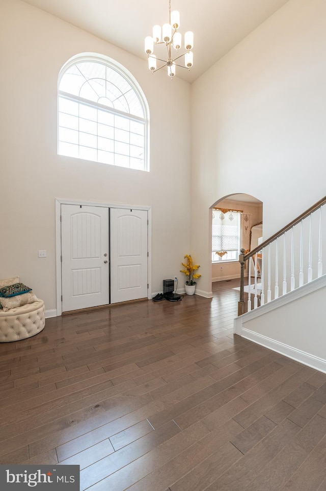 entryway with a notable chandelier, a towering ceiling, and dark hardwood / wood-style floors