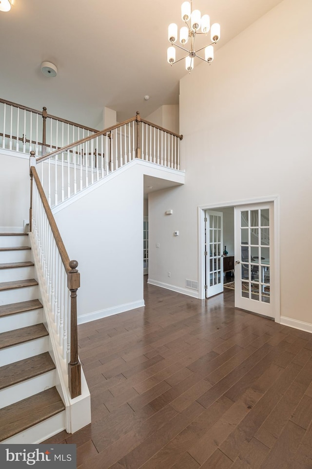 stairway with a notable chandelier, hardwood / wood-style flooring, french doors, and a towering ceiling